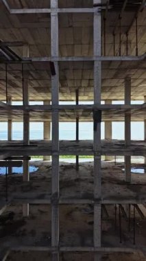 Bir binanın iskelet yapısı yüksektir ve ötesinin büyüleyici deniz manzarası sunar. Güneş ışığı, ham beton ve açık iskeleti vurguluyor..