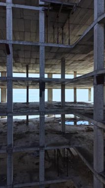 Manzara, sütunları ve açık alanları olan birden fazla katlı beton bir binanın iskelet kalıntılarını ortaya çıkarıyor. Güneş ışığı filtreler, hammaddeleri vurgular.