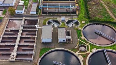 Havadan bakıldığında, yuvarlak ve dikdörtgen tankları olan bir atık su arıtma tesisi, temiz bir gökyüzü altında atık su işlemesi, temiz su yönetiminin önemini vurguluyor..