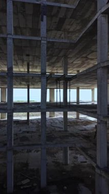 Tamamlanmamış beton sütunlar, okyanus dalgalarına tepeden bakan ıssız bir alanda yerden yükselirken, alacakaranlık sahne boyunca dingin bir ışıltı saçar..