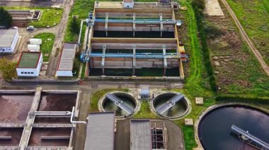 Hava manzarası, yemyeşil ve yollarla çevrili çeşitli depolama tankları ve filtreleme sistemleriyle aydınlık, güneşli bir gökyüzü altında modern bir su arıtma tesisini ön plana çıkarıyor..