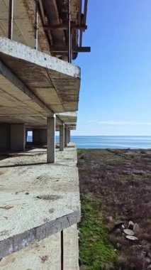 Bitmemiş beton yapı, dingin okyanus sularına ve çevreleyen yeşil karaya göz yumar, berrak bir gökyüzü altında canlı doğaya karşı ihmalkarlığın güzelliğini gösterir..