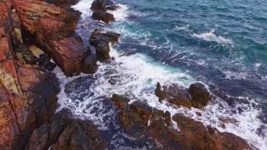 Parlak mavi dalgalar dramatik uçurumlara doğru yükseliyor ve sisli bir püskürme yaratıyor. Güneş ışığı kayaların üzerine sıcak bir ton salıyor, sakin okyanus ise doğanın huzur dolu tefekkürünü ve hayranlığını davet ediyor..