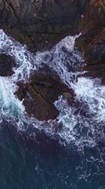 Dalgalar kıyı boyunca engebeli kayalarla çarpışırken altın güneş ışığı suda dans ediyor. Doğanın gücü ve güzelliğinin çarpıcı bir gösterisini yaratıyor..