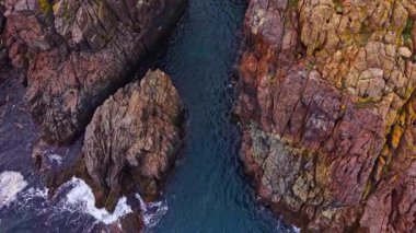 Bu büyüleyici sahne kıyı boyunca dramatik uçurumları yakalar. Sıcak öğleden sonra güneşi altında dalgalar yavaşça kayalara çarparak canlı renkleri ve dokuları aydınlatır..