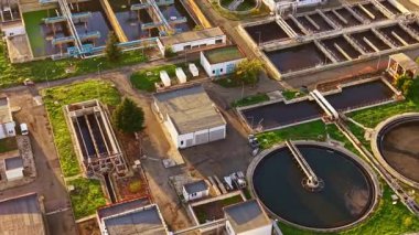 Çemberle çevrili bir su arıtma tesisinin havadan görünüşü, dairesel tanklar ve temiz su, temiz bir ortamda teknoloji ve doğa arasındaki uyumu vurguluyor..