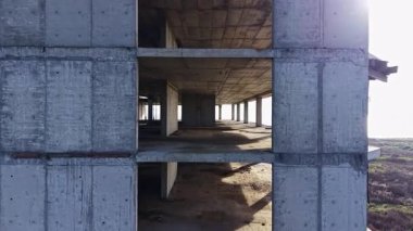 Terk edilmiş bir beton bina okyanus kıyısında duruyor. Açık çizgiler ve boş alanlar sergiliyor. Güneş ışığı açıklıklardan süzülüyor, yere gölge düşürüyor..