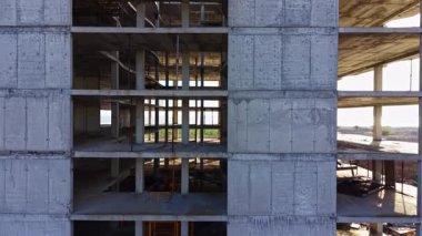 Uzun beton kirişler yukarı doğru uzanıyor ve yeni bir yapının iskeletini ortaya çıkarıyor. Açık alanlardan geçen güneş ışığı filtreleri, devam eden inşaatı vurguluyor.