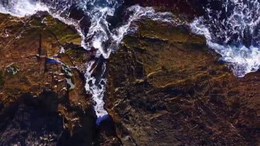 Enerji dalgaları sivri kayalara çarparken parlak güneş ışığı kayalık kıyı şeridini aydınlatır. Sahne doğanın dinamik güzelliğini yakalar, keşif ve yansımayı davet eder..