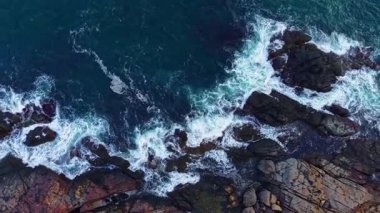 Dalgalar enerjik bir şekilde kıyı şeridi boyunca uzanan karanlık kayalara çarpar. Gün batımında beyaz köpük oluşturur. Gündüzün geceye geçişi gibi çarpıcı bir kontrastla karşılaşır..