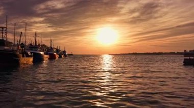 Güneş batarken, onun altın ışığı sakin sulardan yansıyarak limanda huzur içinde demirlemiş bir dizi balıkçı teknesini aydınlatarak sakin bir akşam atmosferi yaratıyor..