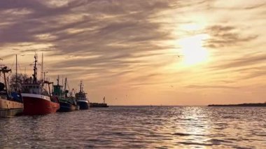 Balıkçı tekneleri limanda huzur içinde dinlenirken renkli günbatımı gökyüzünü boyuyor. Sakin sulara yansıyor. Okyanus fısıltılarıyla dolu güne huzur veren bir son yaratıyor..