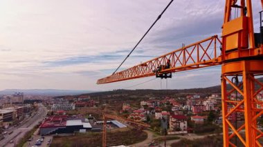 Alacakaranlıkta canlı bir şehir manzarasının üzerinde turuncu bir vinç beliriyor. Aşağıda evler ve işlek sokaklar güneş ufukta batarken şehir yaşamını gözler önüne seriyor..