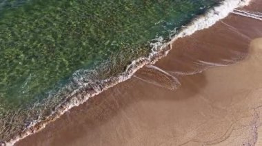 Altın kum berrak turkuaz sularla buluşur. Yumuşak dalgalar kıyıları sarar. Okyanus kıyısında sakin bir akşamın dingin güzelliğini yansıtır..