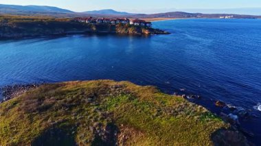 Çarpıcı bir manzara, yumuşak dalgalar ve zengin yeşil bir manzarayla huzurlu bir kıyı şeridini yakalar. Tuhaf pansiyonlar uçurumların tepesinde oturur, doğanın güzellikleriyle çevrili, alacakaranlıkta..