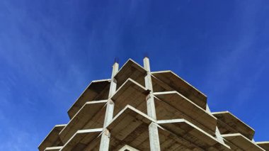 Yukarı doğru yükselen inşaat halindeki beton bina, parlak mavi bir gökyüzünün altında modern mimari ve kentsel gelişimin elementlerini gözler önüne seriyor..