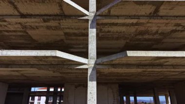 Bitmemiş bir yapıda beton sütunlar dramatik bir şekilde yükselir, aşağıdaki boşlukta cesur gölgeler bırakır, terk edilme ve potansiyel bir hissi uyandırır..