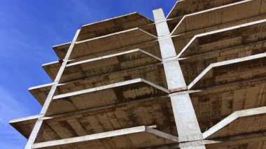 Gök mavisi zemine karşı dik duran bitmemiş beton yapı endüstriyel çekiciliğini sergiliyor, ham sütunlar ve hayata dönüşmeyi bekleyen engin boş alanlar sergiliyor..