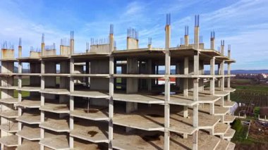 İşçiler tarlalarla çevrili büyük bir bina inşa etmekle meşguller. Uzun beton yapı mavi gökyüzünün arka planında şekilleniyor..