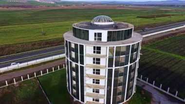 Büyük pencereli çarpıcı yuvarlak bir yapı, batan güneşin altın renklerini yansıtan geniş yeşillikte sessizce oturur. Yakınlarda, bir yol gezginleri bu sakin manzaraya çekiyor..