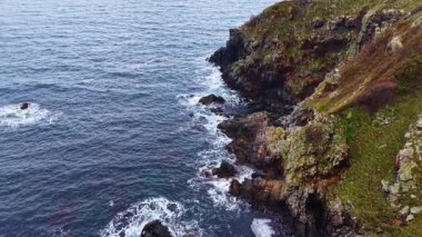 Dalgalar engebeli uçurumlara çarparak doğanın okyanusla buluştuğu sakin bir atmosfer yaratır. Bulutlu gökyüzü, sahneye dramatik bir dokunuş ekler..