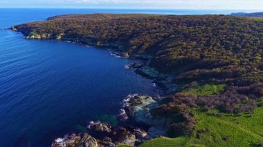 Nefes kesici bir manzara, canlı yeşil karanın sakin denizle buluştuğu engebeli bir kıyı şeridini gözler önüne seriyor. Güneş ışığı suyun üzerinde parıldıyor, doğanın güzelliği arasında keşif ve sükuneti davet ediyor..