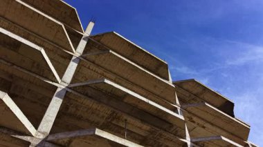 Beton bir otoparkın çarpıcı görüntüsü, açık mavi gökyüzüne karşı yükselir ve eşsiz mimari tasarımının cesur çizgilerini ve şekillerini vurgular..