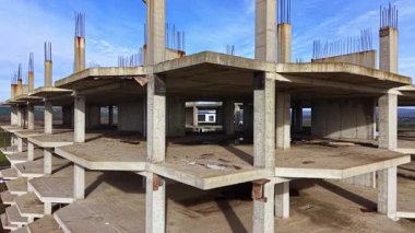 Boş beton kirişler açık gökyüzünün arka planına doğru yükseliyor. Bitmemiş bir binayı sessizce gösteriyor. Yaşamın geri dönmesini bekliyor. Toz, altındaki çorak toprağa yerleşir..