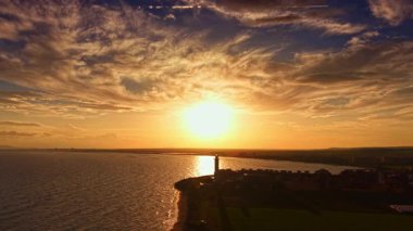 Gün batımı, suyun ufukla buluştuğu huzurlu rıhtım üzerinde altın bir parıltı yayar. Bulutlar turuncu ve pembenin gölgelerini yansıtır ve solan güne sıcaklık katar..