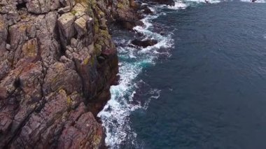 Dalgalar kayalık yüzeylerine çarparken engebeli uçurumlar parıldayan denizden dramatik bir şekilde yükselir. Sahne huzurlu, doğanın güzelliğini bir kıyı ortamında yakalıyor..