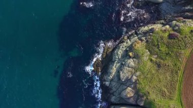 Derin mavi okyanusun kayalık kıyılarla buluştuğu engebeli uçurumları hava manzarası yakalar. Güneş ışığı dalgaların üzerinde dans eder ve yemyeşil alanlar kıyı şeridi boyunca uzanır..