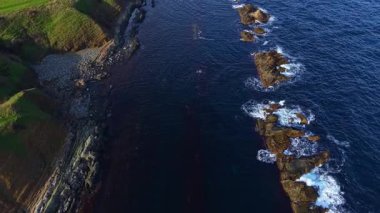 Uçurumlar görkemli bir şekilde yükselirken yumuşak dalgalar kayalık kıyı şeridini öper. Güneş batıyor, manzara üzerine sıcak renkler döküyor, doğal güzelliklerle dolu huzurlu bir sahil sahnesi yaratıyor..