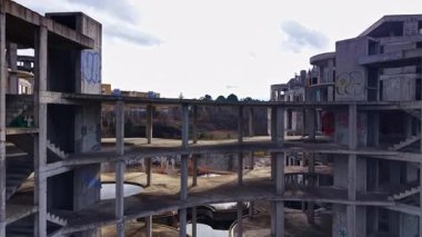 Terk edilmiş, çok katlı beton bir yapı, doğa tarafından sarılmış ve grafiti ile dağılmış olarak duruyor. Bulutlu gökyüzü sahneye kasvetli bir atmosfer ekler ve ürkütücü cazibesini arttırır..