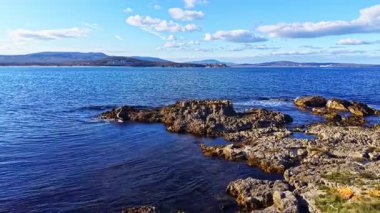 Engebeli kayalara çarpan yumuşak dalgalar sakin bir atmosfer yaratır. Dalgalı mavi su uzak tepelere kadar uzanıyor. Huzurlu bir tefekküre yol açıyor..