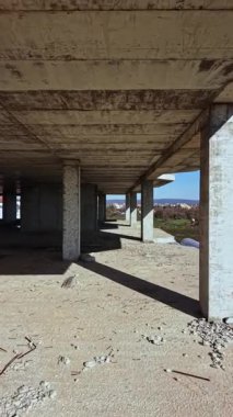 Beton sütunlar, tozlu zeminde uzun gölgeler bırakarak tamamlanmamış bir yapıda dimdik dururlar. Sahne sakin, doğa boş boşluğa bakıyor..