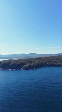 Kıyı şeridi yemyeşil ve nazik dalgaları ortaya çıkarırken parlak güneş ışığı su yüzeyinde dans eder. Huzurlu bir atmosfer, sakin bir yansıma ve doğanın takdir edilmesini ister..