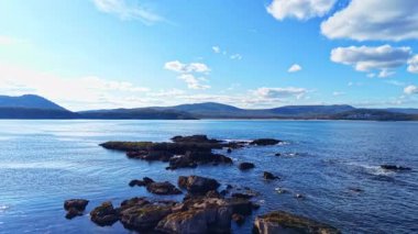 Gözlerden uzak kayalık çıkıntılar bu çarpıcı kıyı manzarasını karakterize eder. Yumuşak dalgalar kıyıya çarpar. Yuvarlanan tepeler ve kabarık bulutlar tarafından çerçevelenir..