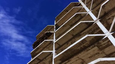 Büyük beton yapı belirgin bir şekilde yükseliyor, endüstriyel güzelliği gözler önüne seriyor. Açık gökyüzü derinlik katıyor, güneşin altında gerçekleşen inşaat işlerinin saflığını vurguluyor..