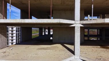 Boş beton yapı, tamamlanmamış bir iç mekanı gösteren bir inşaat sahasında dimdik duruyor. Yeşil alanlar ötesine uzanır, umut verici büyüme ve gelişme.