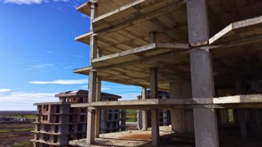 Beton iskeletler, bir zamanlar bu bitmemiş binalara bağlı olan rüyaları ima ederek canlı bir gökyüzüne karşı yükselir. Doğa sessizce çevrelerindeki alanı geri alır..