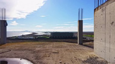 Sahne, engin bir okyanus manzarası oluşturan beton sütunları olan çorak bir inşaat alanını gözler önüne seriyor..