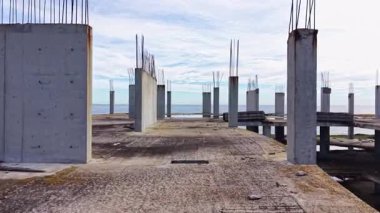 Issız bir kıyı şeridinde çimento sütunları beliriyor. Bitmemiş bir projenin kalıntıları. Okyanus uzakta parlıyor, engebeli sanayi manzarasıyla çelişiyor..