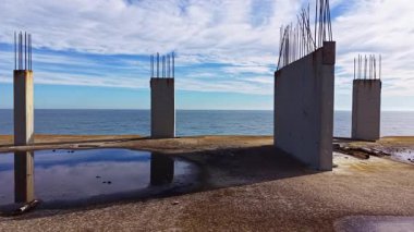 Paslı sütunlar, ıssız bir kıyı şeridinde, geçmişteki inşa çabalarını yansıtırken, kumlu kenarda dalgalar nazikçe dolaşırken, doğa ve insan arasında sakin bir kontrastlık yaratır..