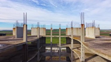 Beton sütunlar uçsuz bucaksız araziye yükseliyor, tamamlanmamış bir yapının çekirdeğini gösteriyor. Güçlendirme çubukları ufuk çizgisini delip geçerek, gelecekteki gelişmeyi ima ediyor.