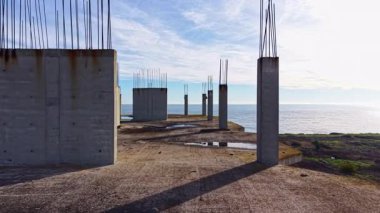 Bu sakin sahil sahnesinde, uzun beton sütunlar sessizce durur, dalgalı gökyüzüne sürtünürler okyanus dalgaları yavaşça kıyıya vurur..