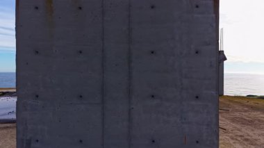 Güçlü beton duvar, güneş batarken sakin denizi görüyor, manzaraya sıcak renkler döküyor ve insan yapımı yapılarla doğanın uyumu vurgulanıyor..