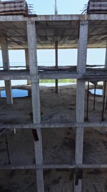 Parlak mavi gökyüzü ve uzak yeşillik tarafından çerçevelenmiş beton sütunlar yerden yükseliyor. Bu bitmemiş yapı sessiz hikayelere ve sıcak bir öğleden sonra şehir keşiflerinin özüne işaret ediyor..