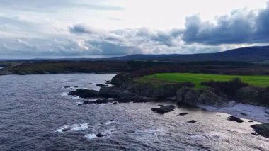 Dalgalar kayalık kıyılara nazikçe yaklaşırken tepeler koyu yeşil uçurumlarla tezat oluşturuyor. Bulutlu gökyüzü, doğanın güzelliğini kucaklayan sakin bir akşamın habercisidir..
