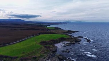 Okyanusun koyu mavi sularıyla birleşen yemyeşil tarlaların çarpıcı manzarası, kıyı şeridi ve tepeler yakınlarındaki alacakaranlıkta huzurlu bir manzara yaratır..