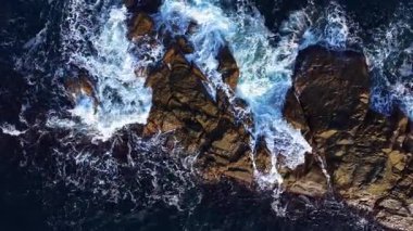 Dalgalar dalgalanır ve kıyı boyunca uzanan sivri kayalara çarparak günbatımının canlı renkleri boyunca su ve taştan büyüleyici bir dans yaratır..